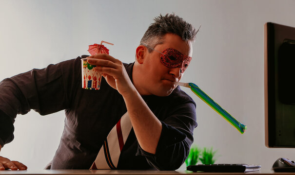 Businessman wearing a party mask drinking alone in office. Alcoh