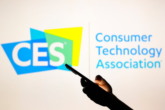 August 1, 2024, Paraguay. In this photo illustration, the Consumer Electronics Show (CES) logo seen in the background with a silhouette hand holding a smartphone.