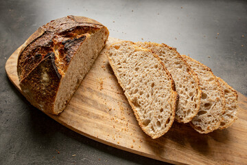 Sourdough bread with slices lies on a wooden board with breadcrumbs around it on a dark worktop