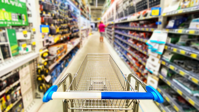 Pusty koszyk, w&oacute;zek sklepowy w supermarkecie, rozmazane tło, wnętrze sklepu, supermarketu, w&oacute;zek na zakupy, p&oacute;łki sklepowe z produktami. Hipermarket.  Miejsce na tekst.