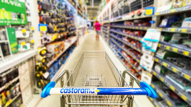 Pusty koszyk, w&oacute;zek sklepowy w supermarkecie, rozmazane tło, wnętrze sklepu, supermarketu, w&oacute;zek na zakupy, p&oacute;łki sklepowe z produktami. Hipermarket Castorama. Warszawa, CH Wola Park. Miejsce na tekst