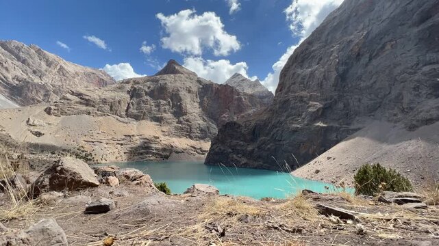 Timelapse view Bolshoi Allo Lake of Fann Mountains in Tajikistan sunny day with clouds. Turquoise high mountain pond surrounded by towering Rocky Cliffs under a vibrant blue sky with scattered clouds
