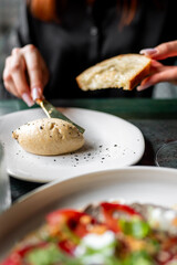 A person spreads butter on a slice of bread at a dining table, with a plate of food in the foreground. The scene captures a cozy, homey atmosphere, perfect for breakfast or brunch settings.