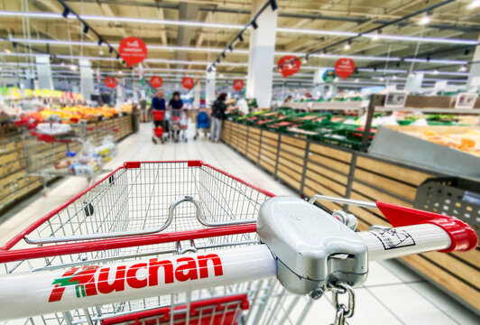 Pusty koszyk, w&oacute;zek sklepowy w supermarkecie, rozmazane tło, wnętrze sklepu, supermarketu, w&oacute;zek na zakupy, p&oacute;łki sklepowe z produktami. Hipermarket Auchan. Warszawa, CH Wola Park. Miejsce na tekst