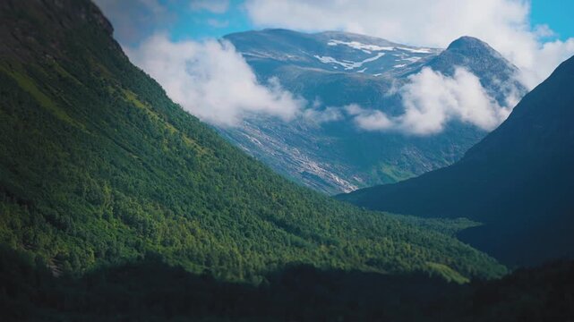 Thin clouds whirl above the wide forest-covered mountainous valley. Aerial view.