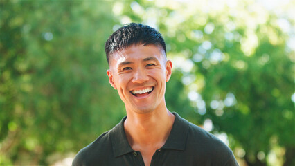 Smiling Man in Green Shirt Enjoying a Sunny Day Outdoors Surrounded by Trees