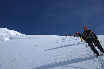 Experienced mountaineers ascend steep snowy slope on a majestic mountain, linked by safety ropes through powdery snow. Teamwork, endurance, and determination in high-altitude climb.