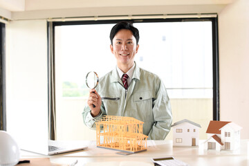 建築模型の前で虫眼鏡を持つ作業服姿の男性 © koumaru