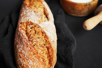 Fresh bread on a black napkin next to a bowl of flour and a wooden rolling pin on a dark background