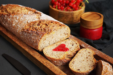 Fresh sliced ​​bread with a heart of berry jam on a wooden tray next to a bowl of red currants and jam on a dark background