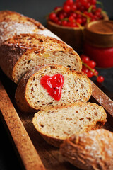Fresh sliced ​​bread with a heart of berry jam on a wooden tray next to a bowl of red currants and jam on a dark background