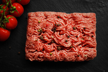 Minced meat with black and red peppers on a black slate tray next to a branch of tomatoes on a dark background