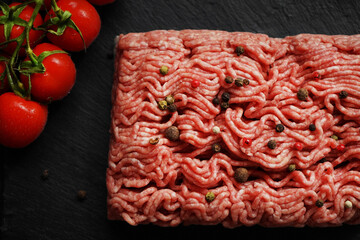 Minced meat with black and red peppers on a black slate tray next to a branch of tomatoes on a dark...