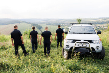 A team of courageous rescuers in black uniforms standing in nature in a field