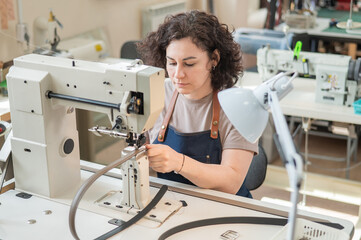 A woman tanner sews a leather belt on a sewing machine. 
