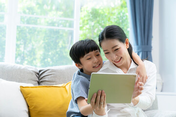 A mother and her 10-year-old son are enjoying a digital tablet together in the living room