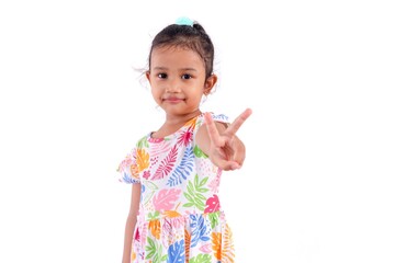 A smiling little Asian girl in a colorful dress showing two fingers or victory sign, on a white background