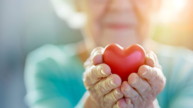 A gentle elderly woman holds a red heart symbolizing love and care, showcasing warmth and compassion in her hands.