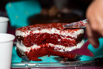 Close-up macro detail shot of the inner slice of a red velvet flavored cake, very brightly colored red and white. While proceeding to cut a slice with a knife and a kitchen spatula