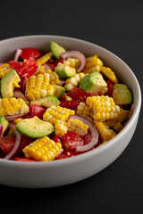 Healthy Fresh Corn Salad in a Bowl on a black background, side view.
