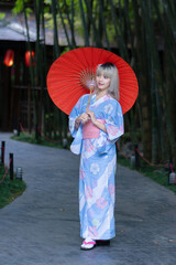 Fototapeta premium Pretty girl in a Yukata dress. A young Asian woman wearing a traditional Japanese kimono or Yukata dress is happy and relaxing with beautiful red maple leaves on the ground in the park.