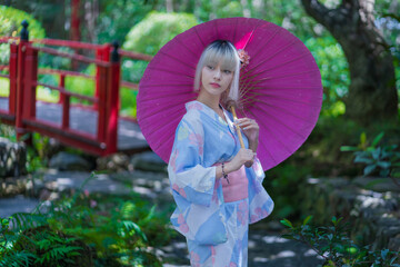 Pretty girl in a Yukata dress.  Portrait fashion young Asian women wearing a traditional Japanese kimono or Yukata dress and holding pink umbrella are happy and relaxing in the fresh green nature.