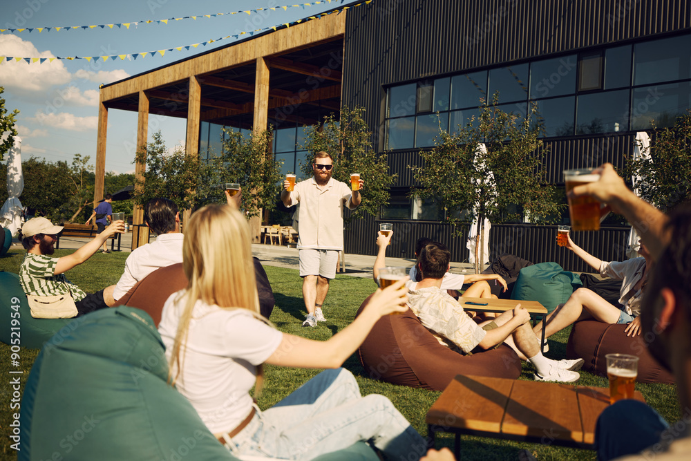 Wall mural Happy young people, friends gathering in outdoor cafe space, having outdoor picnic with refreshing beer and cheerful talks. Concept of summer, leisure, friendship, meeting, fun, relaxation