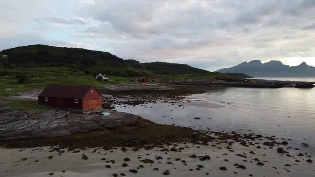 Red wooden hut cabin on a Northern Norway beach during midnight sun in summer with reflection on water