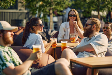 Lively Picnic. Young people, men and women, friends gathering on outdoor restaurant space, cheerfully talking and drinking beer. Concept of summer, leisure, friendship, meeting, fun, relaxation