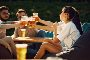 People meeting for a picnic, friends sitting together and drinking beer, clinking glasses, sharing joy and good conversations. Concept of summer, leisure, friendship, meeting, fun, relaxation