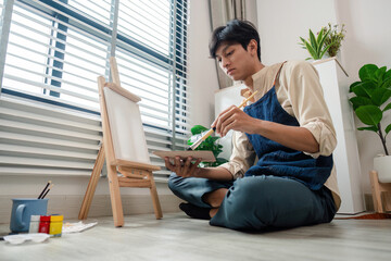 Young Man Painting on Canvas at Home in a Bright Room with Natural Light and Indoor Plants