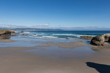 Wide shot of a sandy beach with calm waves and rocky outcrops. Coastal and ocean landscape concept