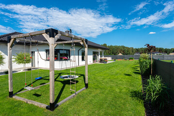 Beautiful garden with green grass, visible terrace table and house in beautiful summer weather, very wide shot.