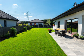 Beautiful garden with green grass, visible terrace table and house in beautiful summer weather, very wide shot.