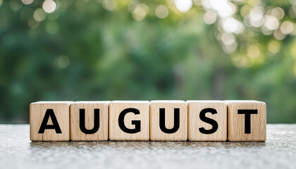 Wooden cubes with word AUGUST against green plant background. Summer time. Travel and vacation