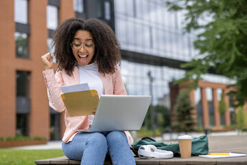 Ecstatic african american woman student rejoices upon receiving good news while sitting outside...