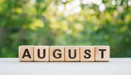 Wooden cubes with word AUGUST against green plant background. Summer time. Travel and vacation