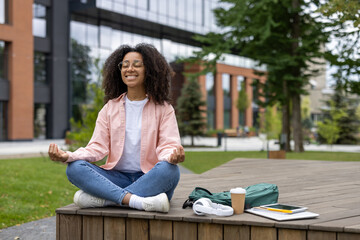 Young African American woman meditating outdoors, sitting cross-legged on wooden platform in urban...