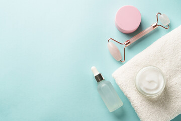 Skin care products. Cream jar, jade roller and serum bottle on blue background. Flat lay with copy...