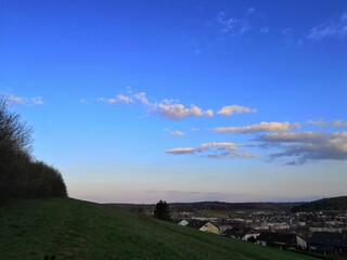 Himmel mit angedeutetem Sonnenuntergang, einem H&uuml;gel und Kleinstadt, am Abhang