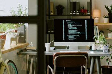 No people shot of modern desktop computer with code on screen on desk in modern eco-friendly office interior