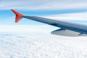 Obraz premium Long airplane wing with red fin high up in the sky. View from plane, travel and transportation