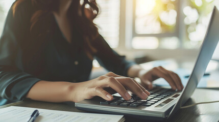 A woman works on a laptop in a sunlit room, her fingers typing on the keyboard, surrounded by a warm, productive ambiance.