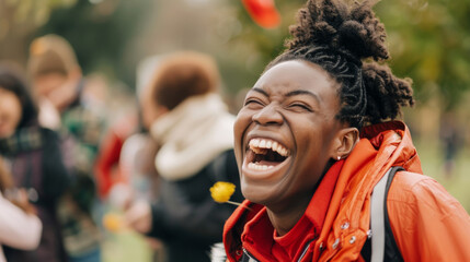 Obraz premium A woman laughing heartily, outdoors, with people and greenery in the background, capturing a moment of pure joy and happiness.
