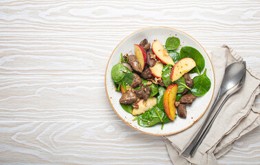 Healthy Salad with Iron Rich Ingredients Chicken Liver, Apples, Fresh Spinach and Walnuts on White Ceramic Plate, White Wooden Background From Above Space For Text.