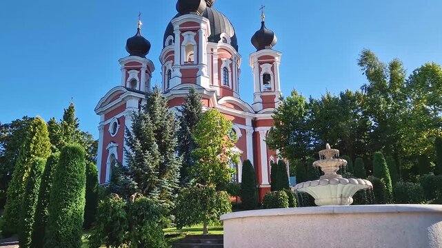 Young woman walks in the gardens of Curchi Monastery with outdoor view to the water fountain. Christian Orthodox church with a beautiful green yard located in Orhei, Moldova