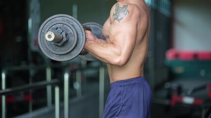 A shirtless man with a tattoo lifting a barbell in the gym, highlighting strength, fitness, and dedication in a focused workout session.
