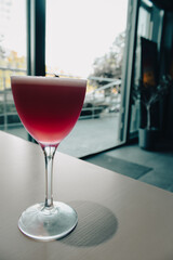 Cosmopolitan cocktail on the table. Elegant glass of red cocktail in empty cafe. Cold drinks concept. Summer cafe interior. Icy alcohol cocktail. Big city lifestyle.