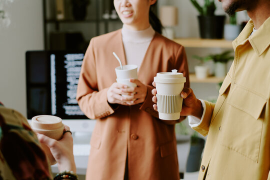 Group of unrecognizable young people holding reusable cups having coffee break at work in office