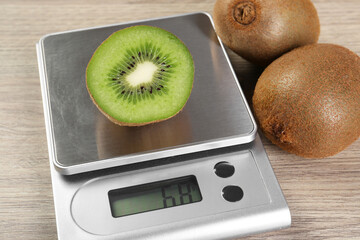 Kitchen scale with piece of kiwi on light wooden table, closeup